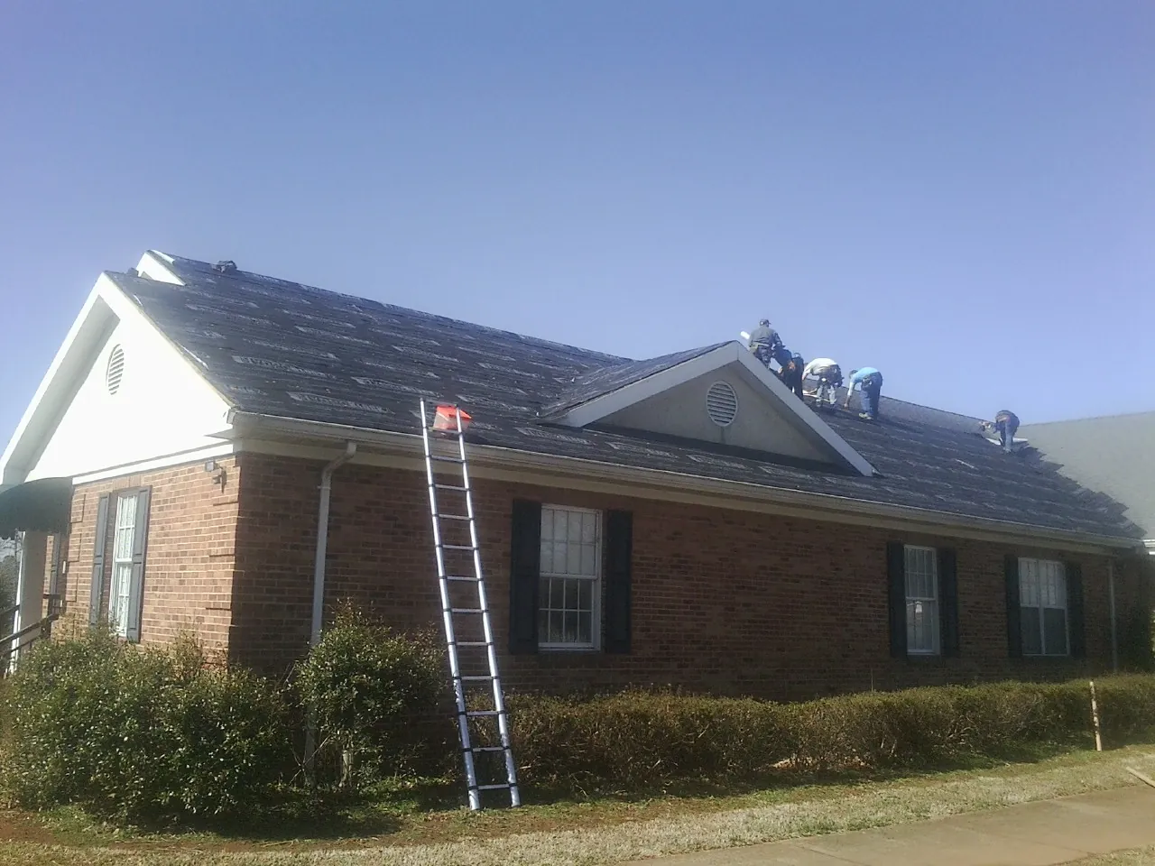 Crew tearing shingles off a brick ranch roof with a ladder set — Metal Roof Repair work by our crew in Crawfordsville