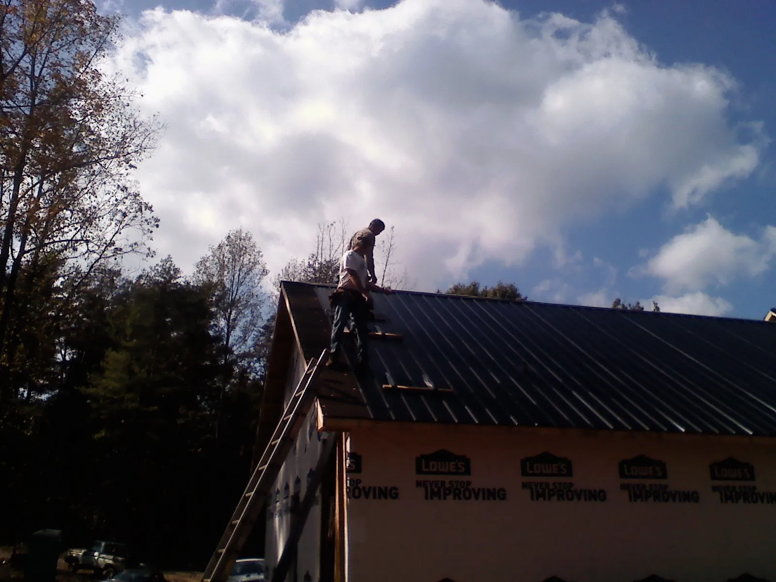 Roofer fastening dark metal panels high against a cloudy sky, from a Roof Inspection job in Crawfordsville
